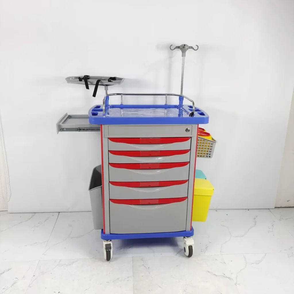 Hospital emergency cart with red drawers, blue tray, IV stand, and waste bins, positioned against a white wall on a marble floor.