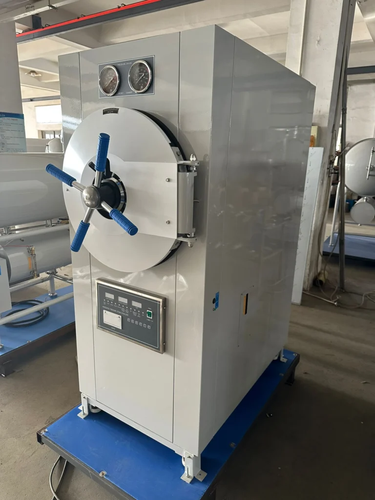 Large industrial autoclave machine with pressure gauges and control panel, situated in a factory environment.