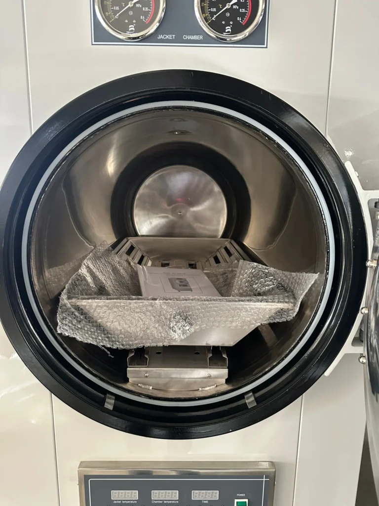 Interior of an industrial autoclave with gauges, showing a tray lined with bubble wrap inside the chamber.