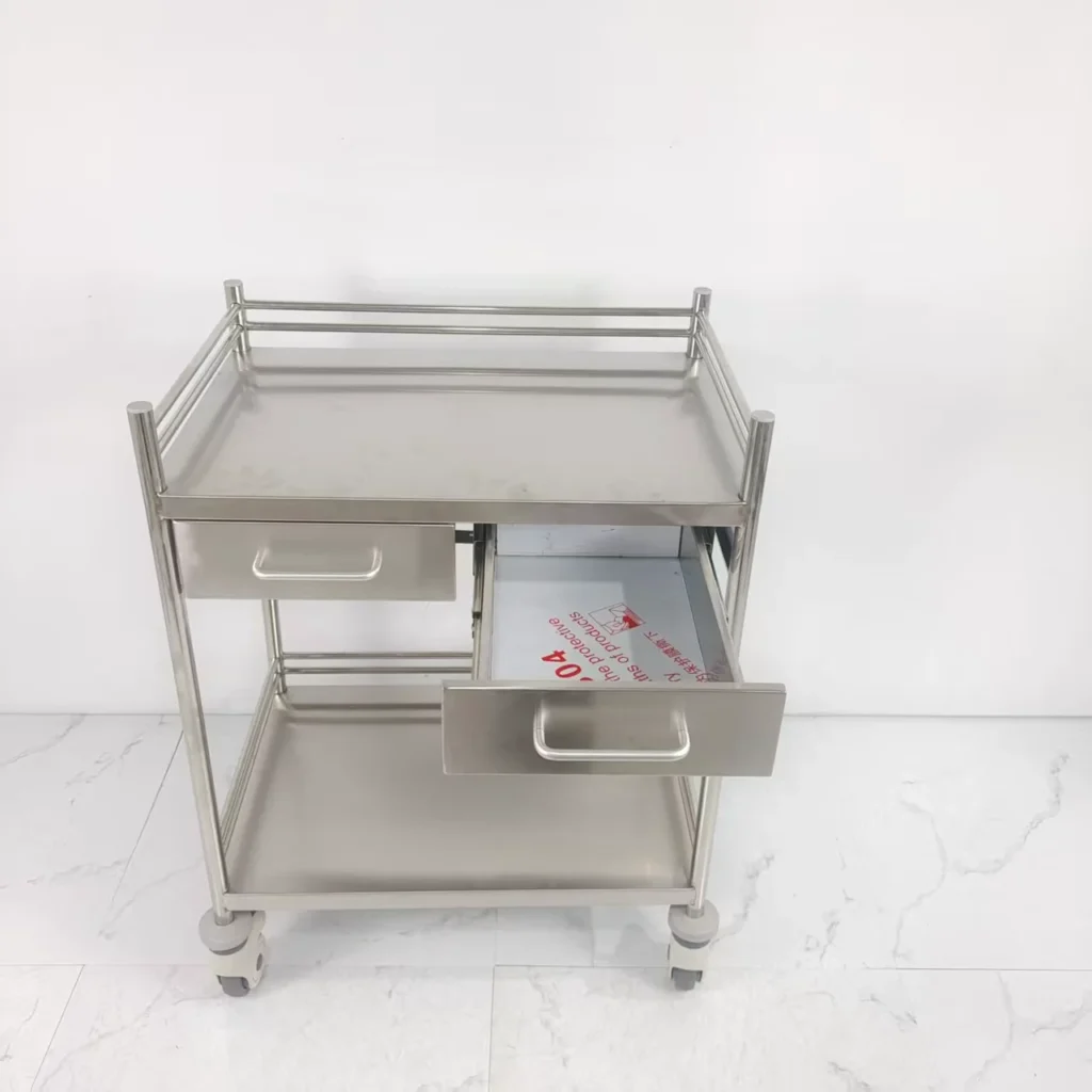 Stainless steel medical utility cart featuring two open drawers and caster wheels, situated against a plain white backdrop.