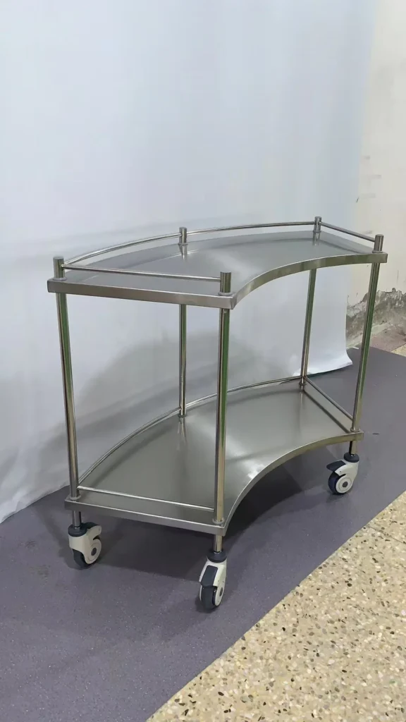 Stainless steel serving trolley with a curved design and four wheels on a purple and terrazzo floor.