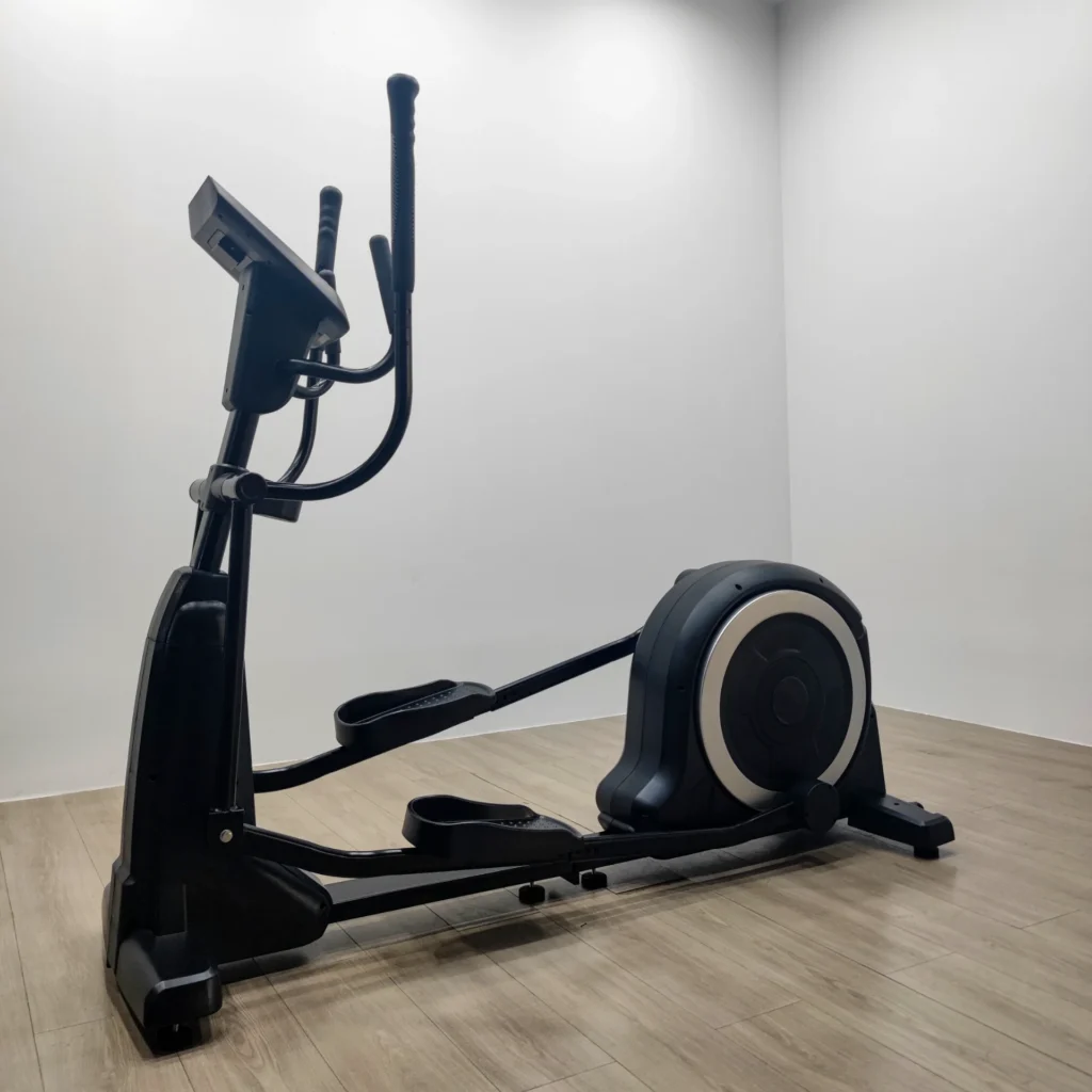 Elliptical trainer in a corner of a fitness room with wooden flooring and white walls.