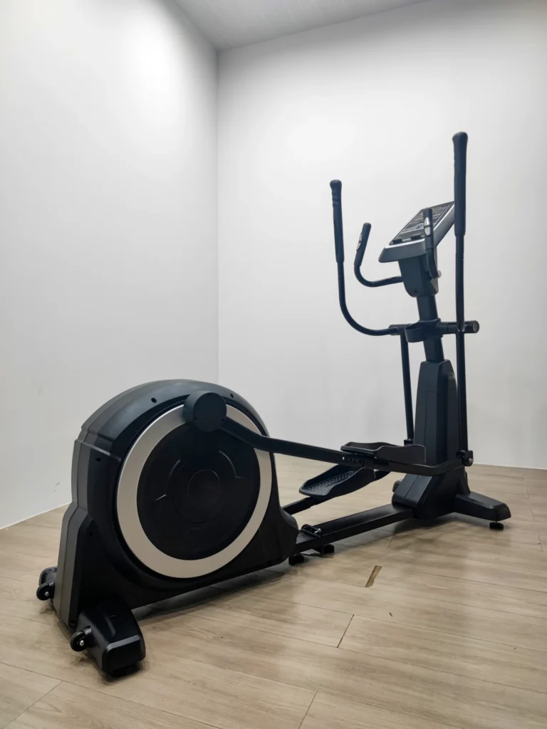 Black elliptical trainer positioned in a bright, modern room with wooden flooring and white walls.