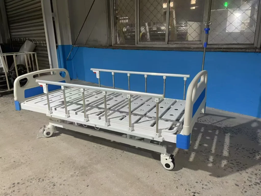 Adjustable hospital bed on wheels with side rails, located indoors with blue and grey walls.