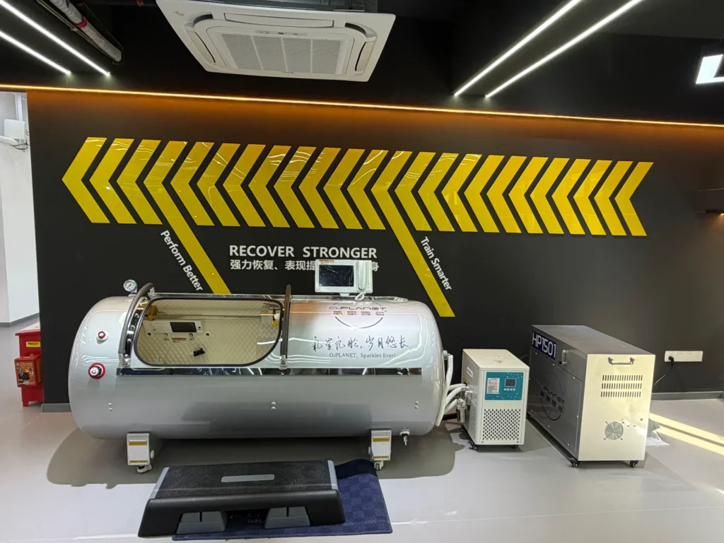 Hyperbaric chamber setup in a recovery room with motivational text on the wall and surrounding equipment for enhanced performance.