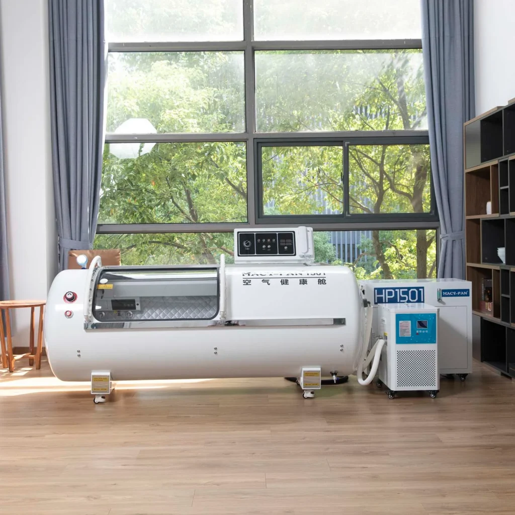 White hyperbaric chamber setup in spacious room with large window, hardwood floors, and blue curtains; trees visible outside.