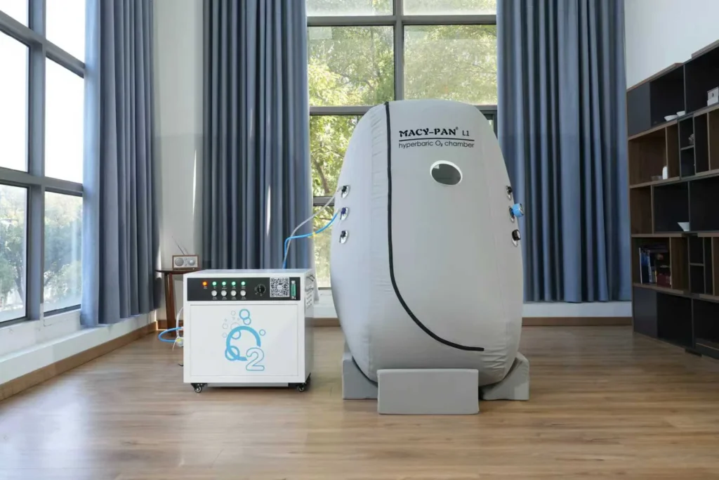 Macy-Pan L1 hyperbaric oxygen chamber situated indoors next to an oxygen generator in a modern room with wooden floors.