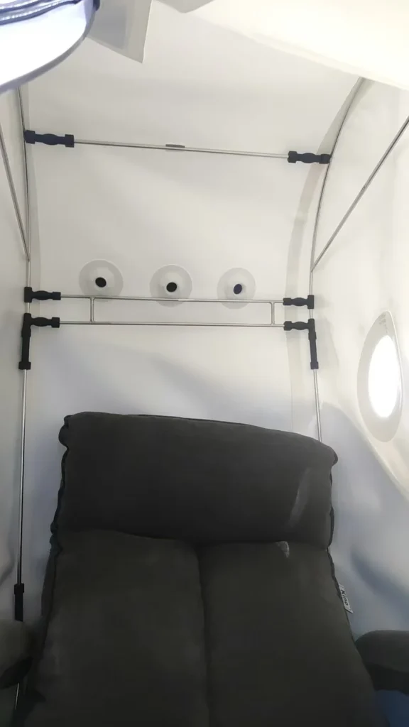 Interior view of an airplane seating area featuring a cushioned seat, small windows, and overhead panel with air vents.
