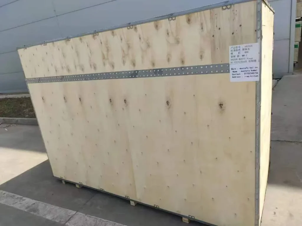 A large wooden shipping crate on a concrete surface, displaying a label with shipping details.