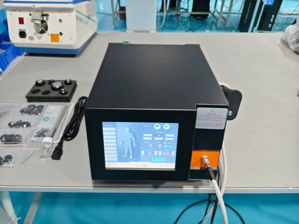 Medical device with digital interface displaying a human figure, placed on a table with various components and wires.