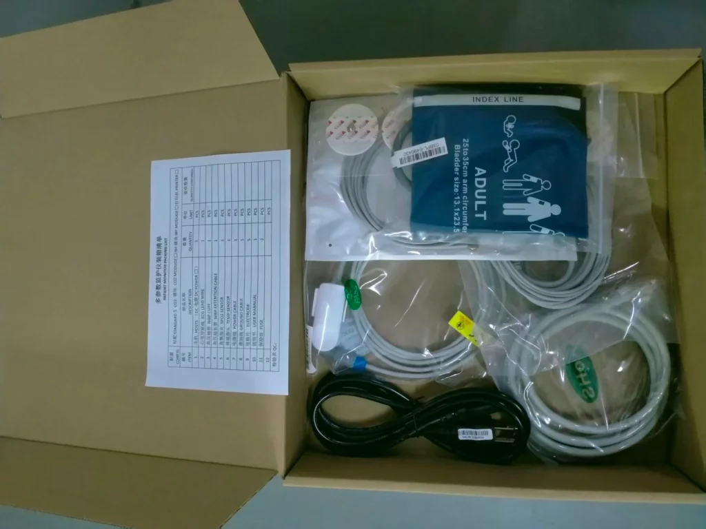 Open box containing medical equipment cables, an adult blood pressure cuff, and other accessories with a contents list attached.