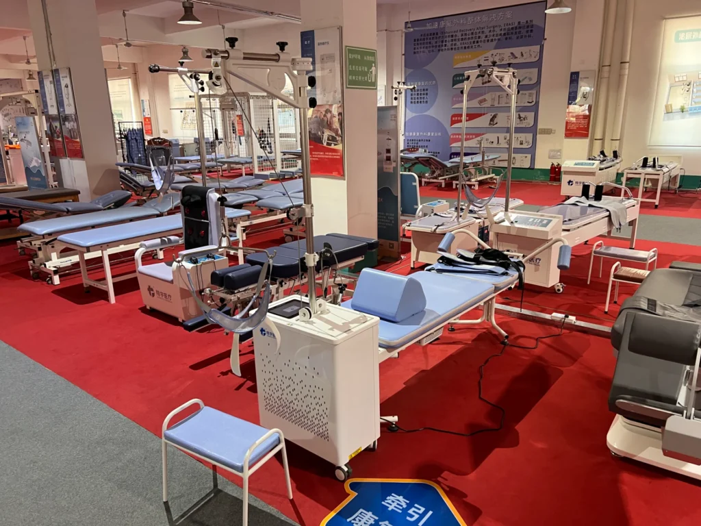 Medical rehabilitation equipment including therapy tables and machines displayed in an exhibition setting with red carpet.