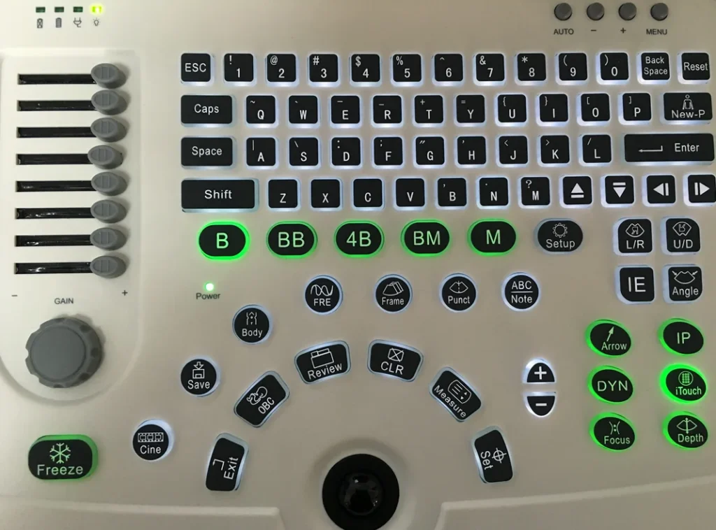 Close-up of a medical imaging control panel showing various buttons and controls, including a keyboard, sliders, and labeled function keys.