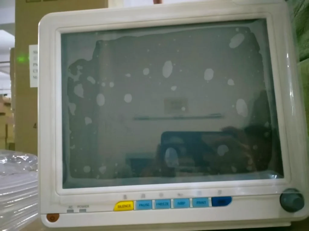 Old medical monitor with buttons for silence, pause, freeze, NBP, and print, stored in a room with boxes.
