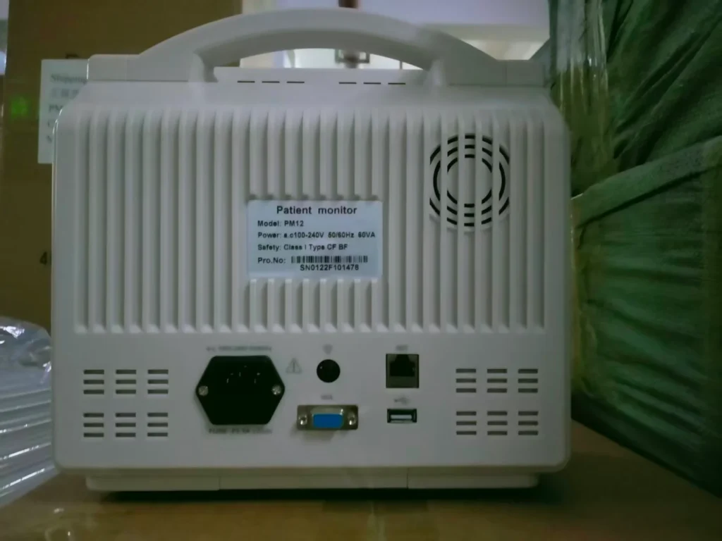 Back view of a white patient monitor device showing ports, model PM12, and power specifications.