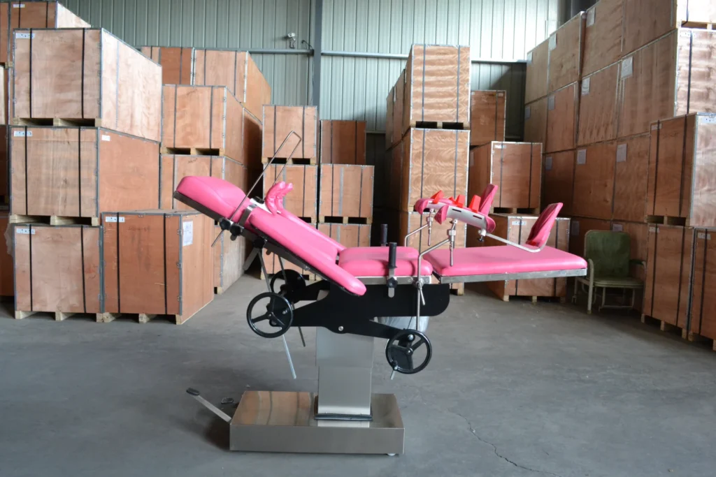 Pink medical examination table with wheels inside a warehouse filled with wooden crates.