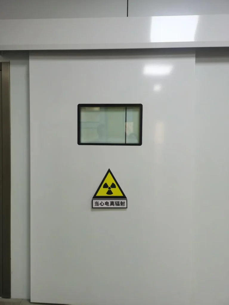 White sliding door with a radiation warning sign and a small window, indicating a restricted area.