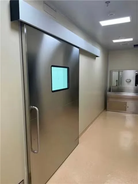 Stainless steel sliding door with a window in an industrial facility corridor, featuring bright lighting and a clean environment.