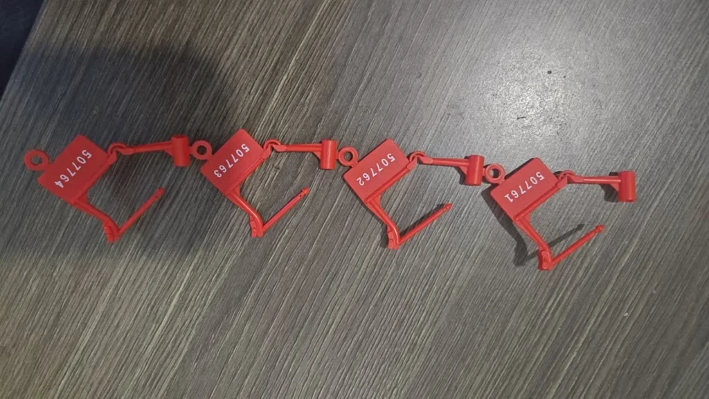 Four red plastic security seals with serial numbers arranged on a wooden table.