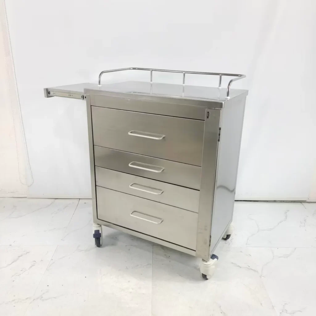 Stainless steel medical cart with four drawers, a side pull-out tray, wheels, and a guard rail on top against a white background.