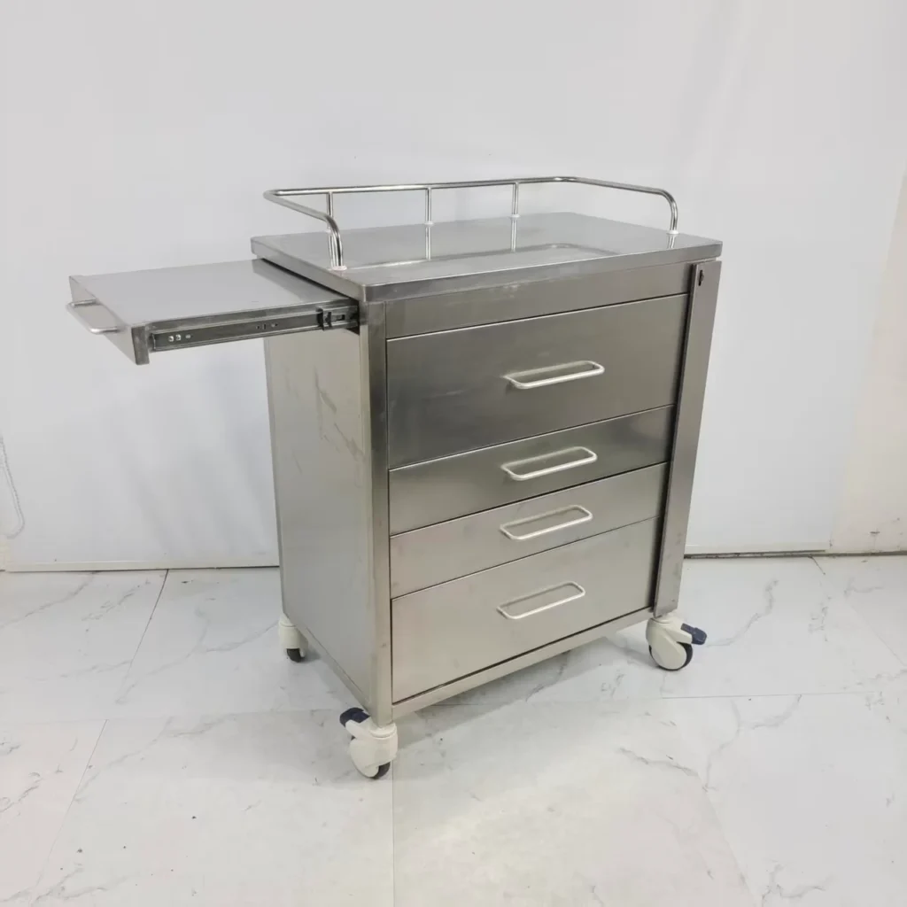 A stainless steel medical trolley featuring four drawers, a side pull-out tray, and wheels for mobility, placed on a tiled floor.