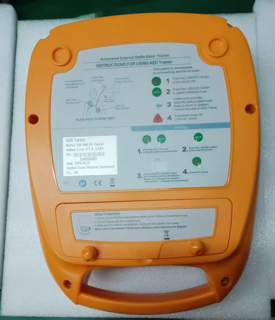 Close-up of an AED trainer device showing labeled usage instructions, settings, and information about the model and manufacturer.