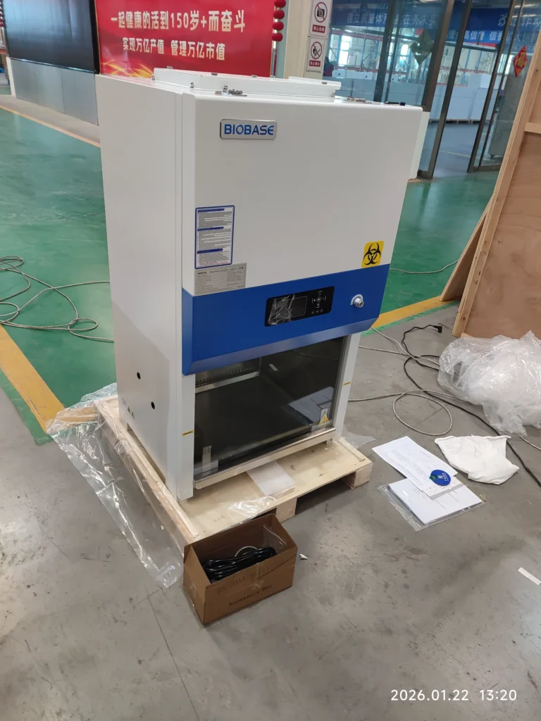 Biobase biosafety cabinet placed on a wooden pallet in a factory setting, surrounded by packaging materials and instruction sheets.