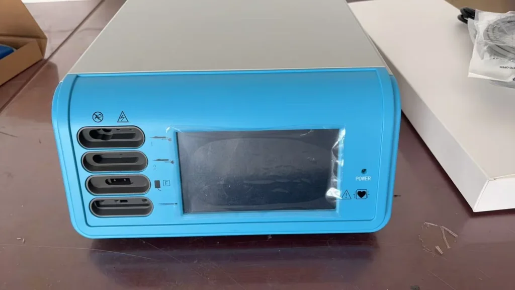 Blue medical device console with an LCD display and multiple ports on a table surface.