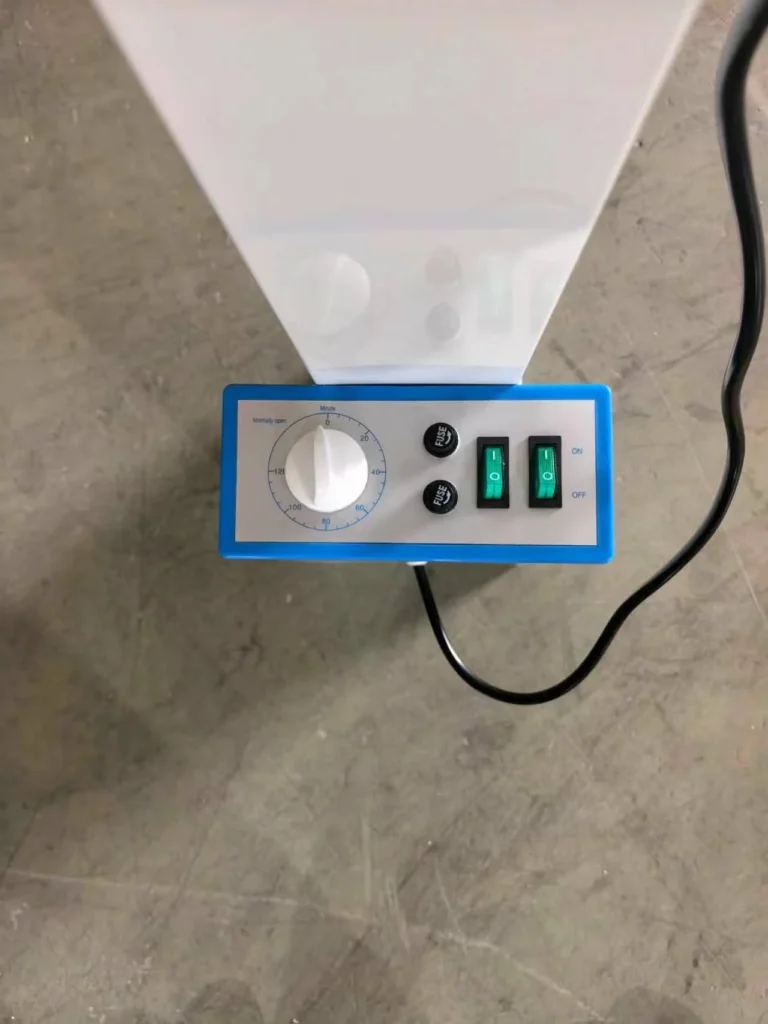 A control panel featuring a white knob with a timer dial, two green on/off switches, and two fuse holders on a gray and blue base, placed on a concrete surface.