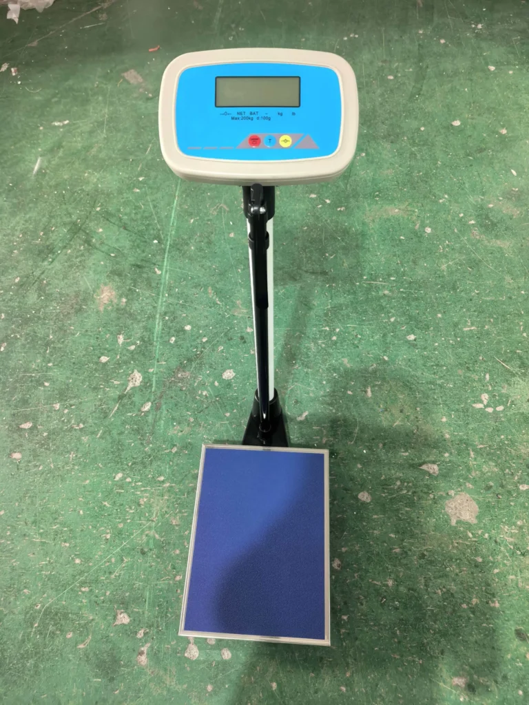 Digital scale with a stand and a blue display screen on a green floor, including a blue weighing platform.