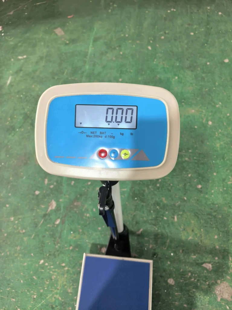 Digital weighing scale with an LCD display showing 0.00, placed on a green textured floor.
