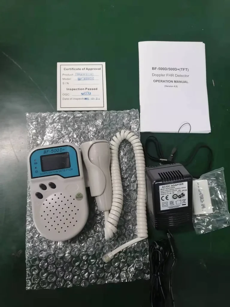 Complete Doppler FHR detector kit including the device, probe, AC/DC adapter, inspection certificate, and user manual laid out on a green surface.