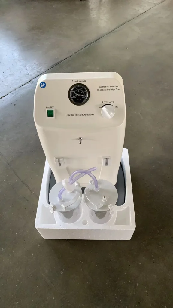 White electric suction apparatus with pressure gauge, regulator knob, on/off switch, and two connected canisters, placed on a styrofoam base.