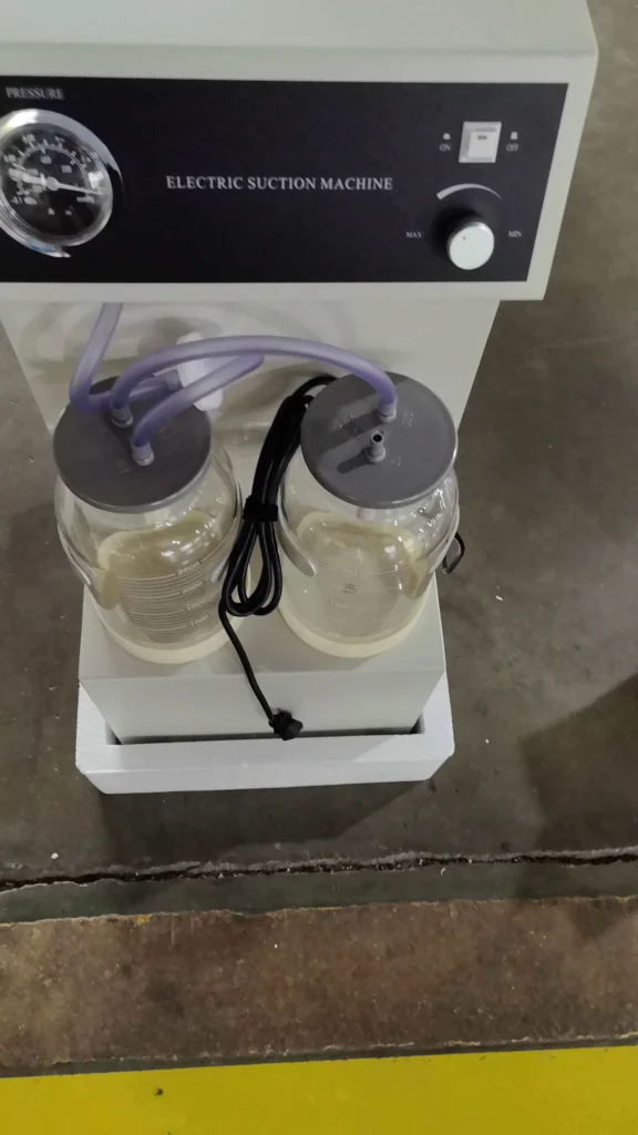 Dual-jar electric suction machine with pressure gauge and controls on a flat surface.