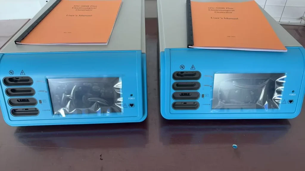 Two blue electrosurgical generators with user manuals placed on top, displayed on a wooden surface.