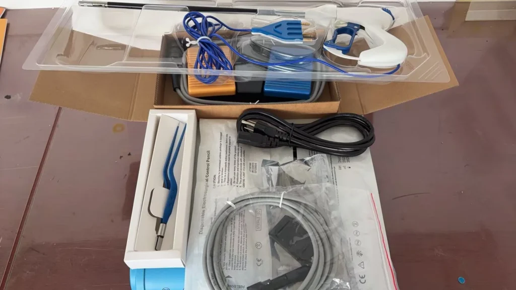 Open box containing an electrosurgical instrument kit with various components, including cables, control pencil, and medical accessories.