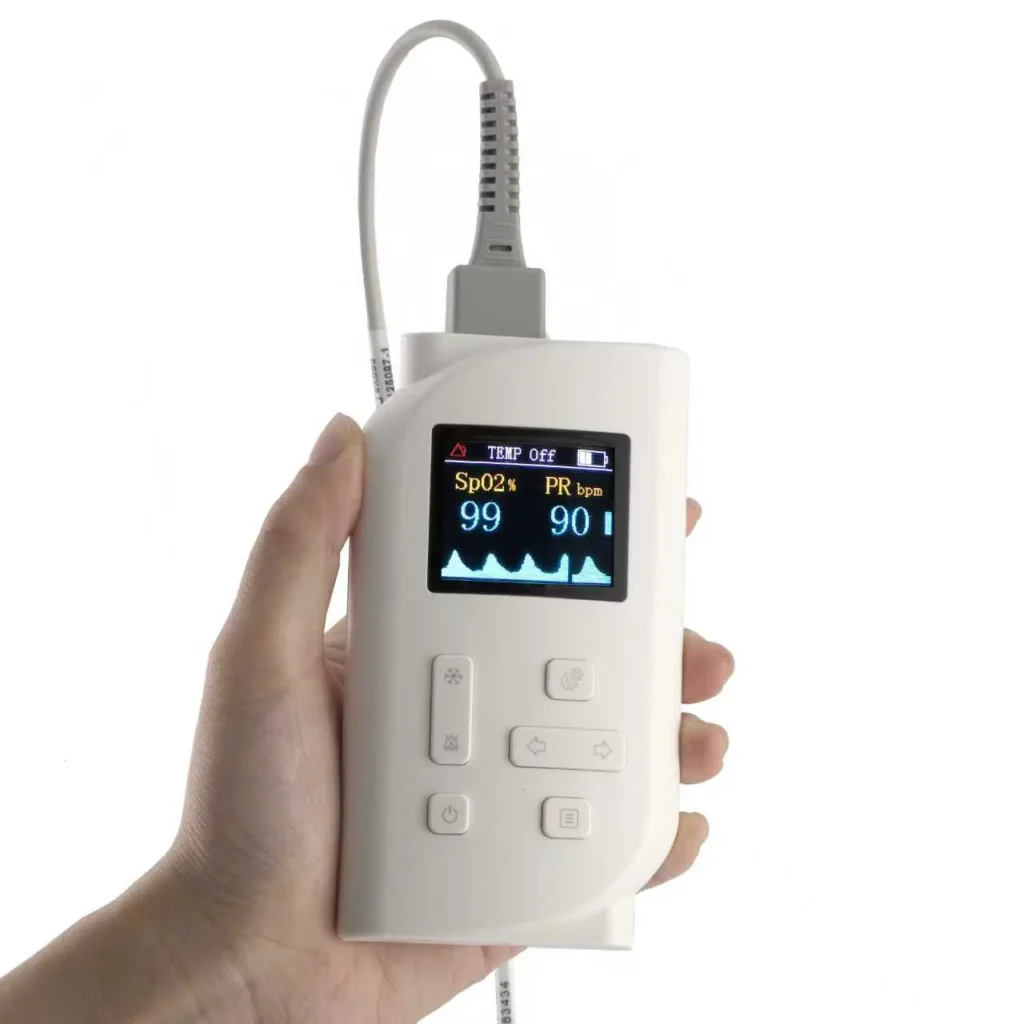A hand holding a portable white pulse oximeter measuring SpO2 and pulse rate with a visible display screen and control buttons.