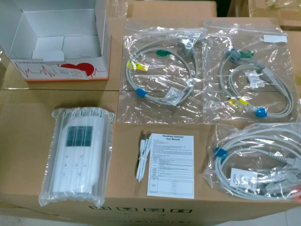Handheld oximeter with user manual, cables, and packaging displayed on a cardboard box.
