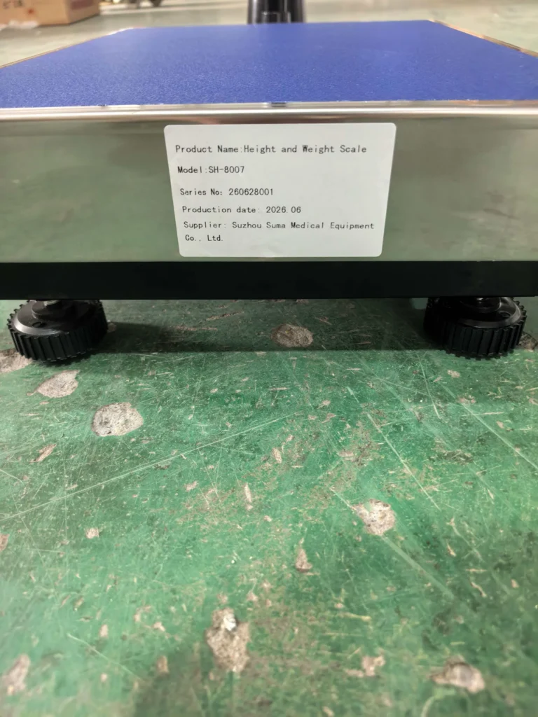 Close-up view of a height and weight scale platform with a sticker showing product details including model, series, production date, and supplier information.
