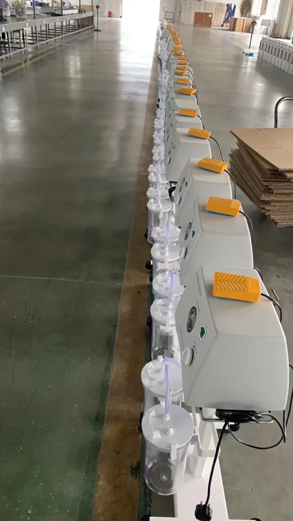 Row of white industrial vacuum machines with cylindrical containers and orange handles, arranged in a factory setting.