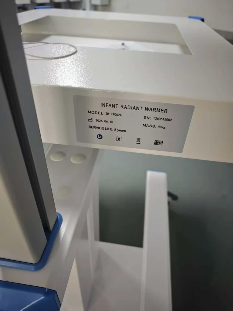 Close-up of a label on an infant radiant warmer showing model number SW-IW002A, serial number, service life, and mass.