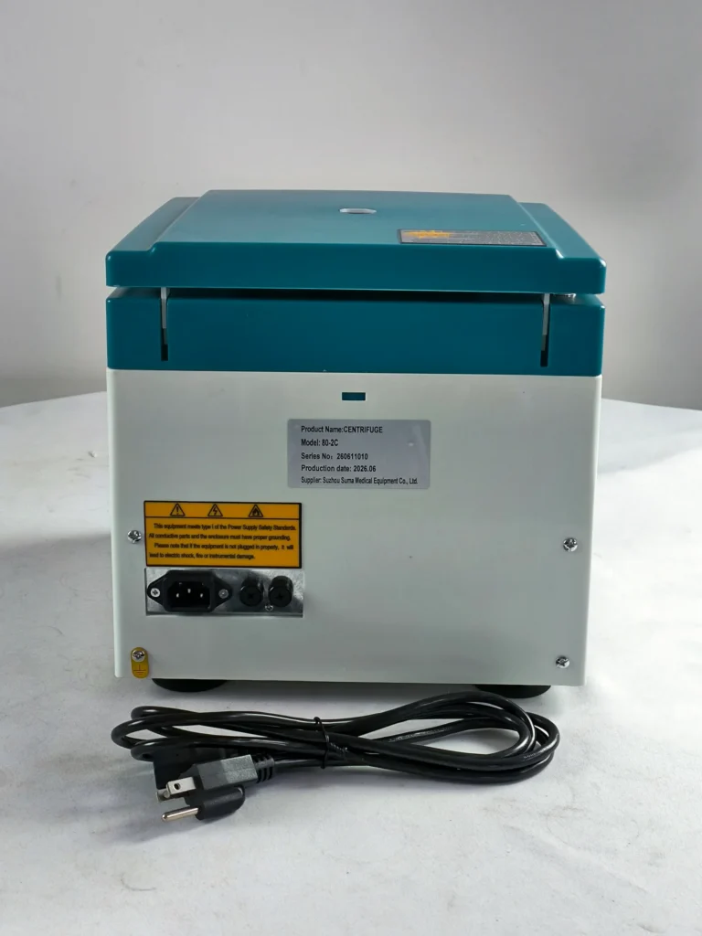 Back view of a laboratory centrifuge showing the power input, labels, and a coiled power cord on a white surface.