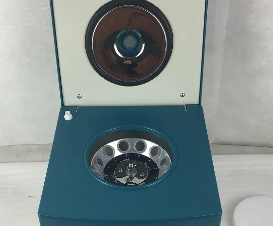 An open laboratory centrifuge machine with a teal casing, metallic rotor, and white interior setup on a light surface.