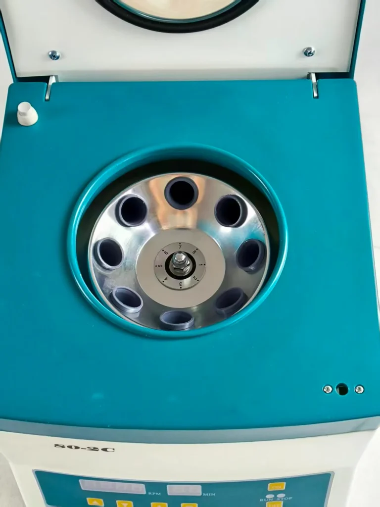 Close-up view of a laboratory centrifuge machine with an open lid, showing a rotating chamber with multiple tube slots.