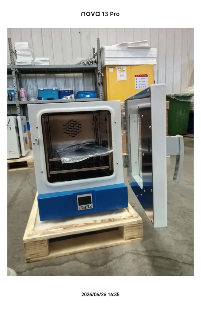 A laboratory oven with an open door placed on a wooden pallet in an industrial setting, showing interior racks and digital controls.