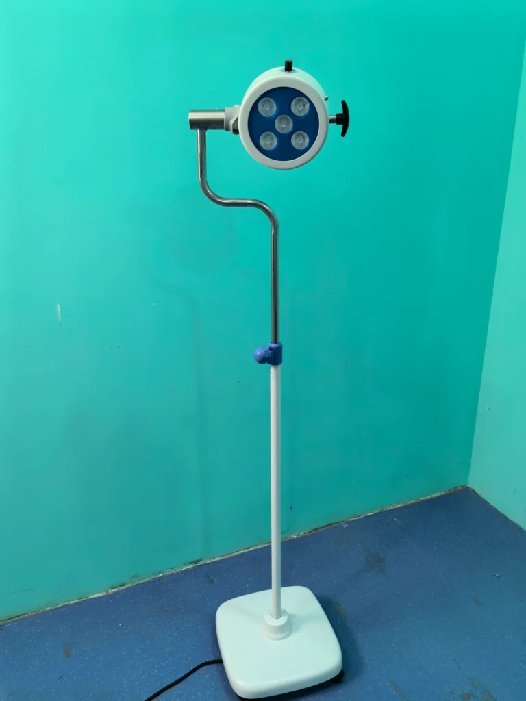 Medical examination light with an adjustable stand and a circular light head, positioned in a blue and teal room.