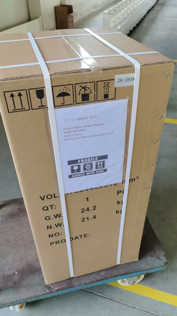 Cardboard box containing a suction machine, labeled with product and shipment details, placed on a warehouse trolley.