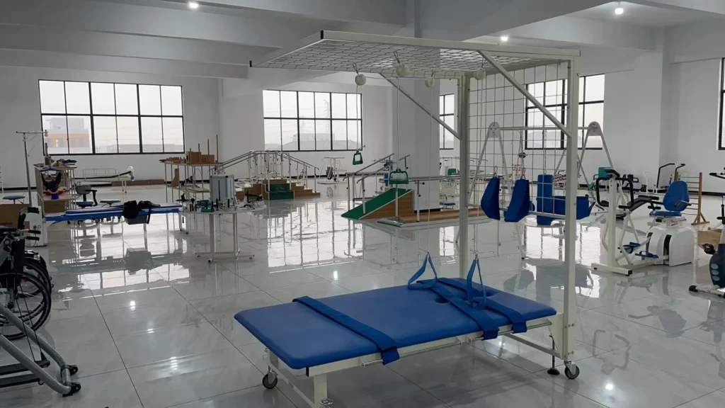 A spacious physical therapy clinic featuring rehabilitation equipment, including blue treatment tables, exercise machines, and mobility aids.