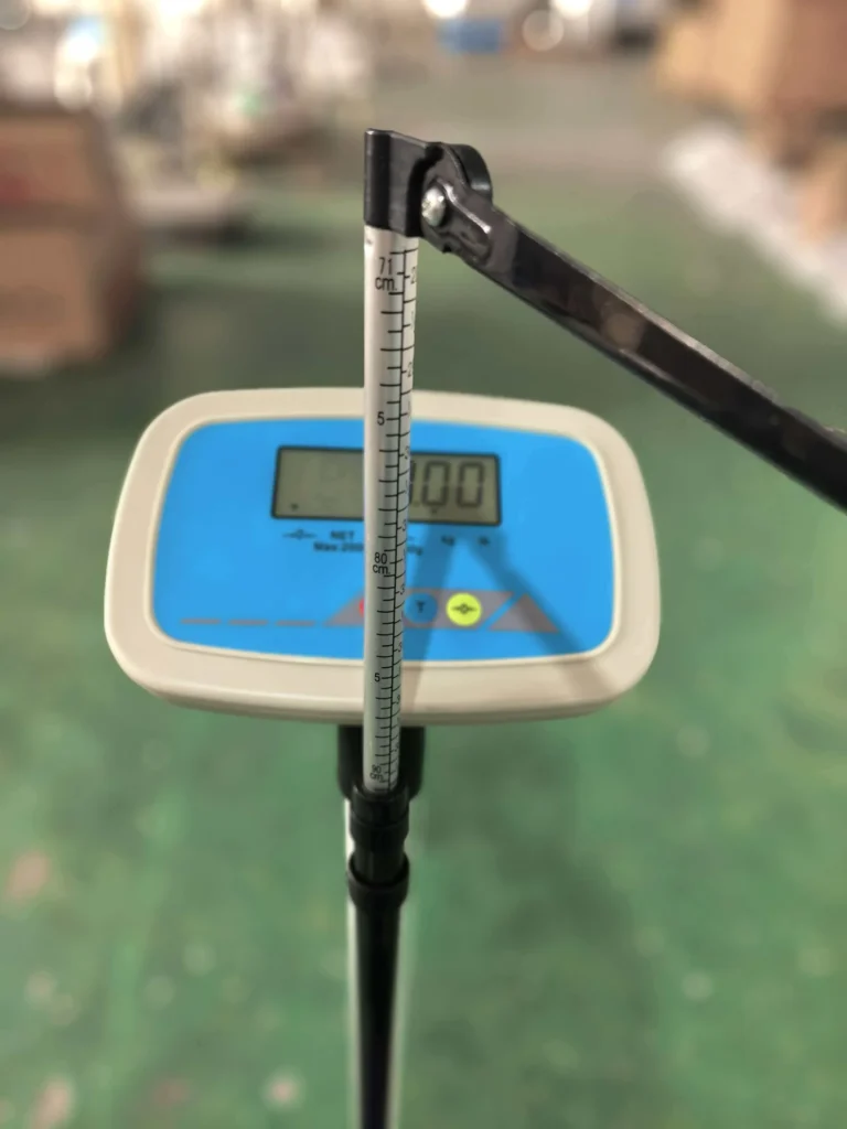 A close-up of a portable digital height measurement scale with a blue screen showing numbers and a height ruler attached.