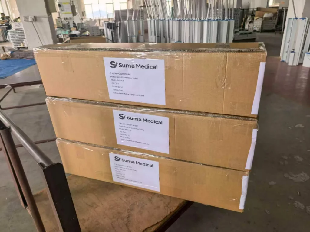 Stacked cardboard boxes labeled with 'Suma Medical,' placed in a warehouse with equipment visible in the background.